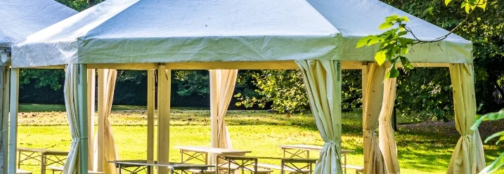 Ein weißes Gartenpavillon mit Bierzeltgarnituren darunter.